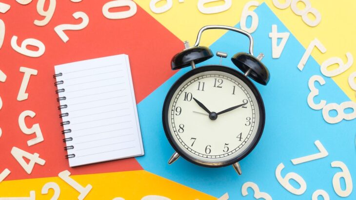 A notebook and an alarm clock surrounded by white numbers on a colourful background.