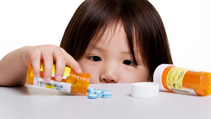 A small child empties a prescription bill bottle on to a counter.